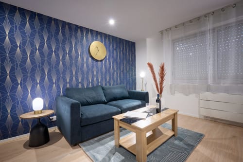 Modern studio apartment in Bordeaux with blue patterned wallpaper, dark sofa, wooden table, and decorative accents
