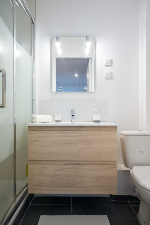 Modern bathroom in Bordeaux studio apartment with wooden vanity, illuminated mirror, and black tile flooring