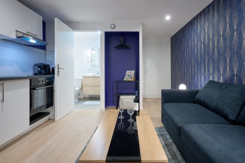 Modern studio apartment in Bordeaux with open-plan kitchen, living area, dark sofa, and blue accent wall