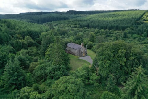Stone chapel nestled in lush green forests of Monaghan, Ireland, surrounded by dense woodland and rolling hills.