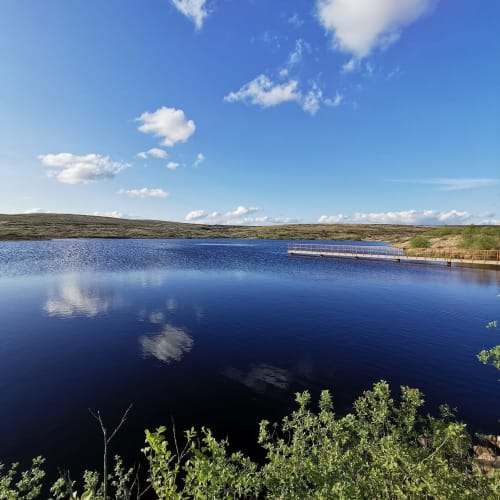Serene lake view at Sliabh Beagh Hotel with blue water, walking pier, rolling hills, and white clouds under clear sky in