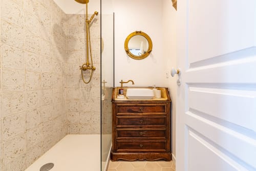 Elegant bathroom at La Maison George with vintage wooden vanity, brass fixtures, and cream tile shower enclosure