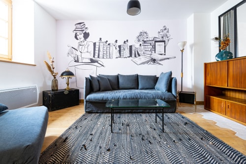 Salon moderne de La Maison George avec canapé bleu, décoration murale littéraire, mobilier bois et tapis géométrique à Flavigny sur