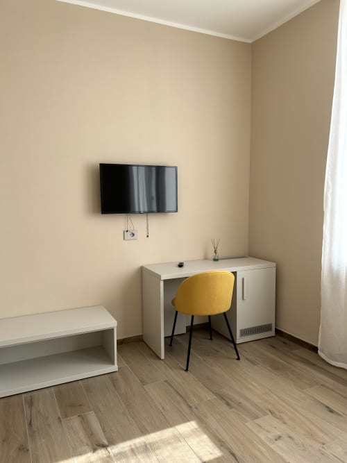 Camera moderna dell'hotel Breccia nel Mare con scrivania, sedia gialla, TV a parete e pavimento in legno a Marina di Carrara