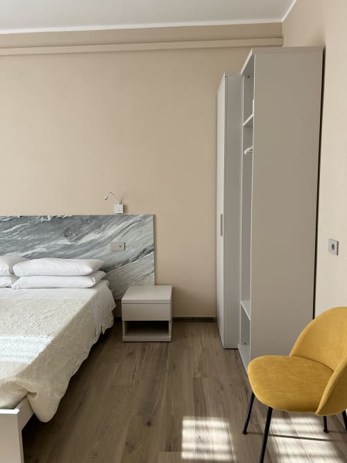Camera moderna presso il Breccia nel Mare B&B a Marina di Carrara con testata in marmo, biancheria bianca, sedia gialla e armadio