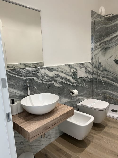 Bagno moderno presso Breccia nel Mare a Marina di Carrara con piastrelle in marmo, lavabo da appoggio, bidet e box doccia