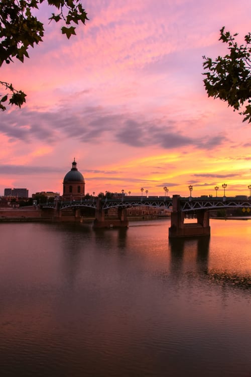 Coucher de soleil sur le Pont Saint-Pierre de Toulouse avec le dôme emblématique et reflets du pont dans l'eau