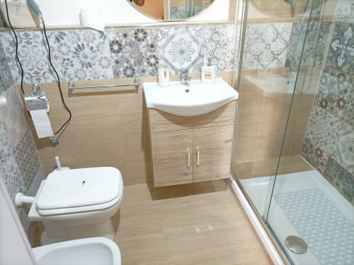 Bagno moderno della villa Newhouse a Bari con vanità in legno, rivestimento decorativo in piastrelle e doccia in vetro