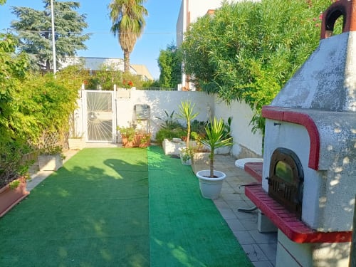Villa Newhouse a Bari con prato verde, piante in vaso, cancello bianco e architettura tradizionale con dettagli rossi