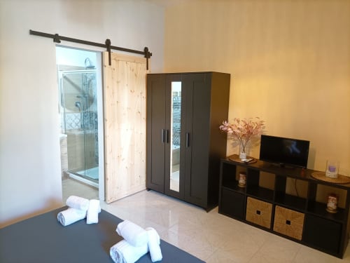 Camera da letto moderna a Newhouse Bari con armadio scuro, mobile TV e bagno ensuite visibile attraverso porta in stile barn