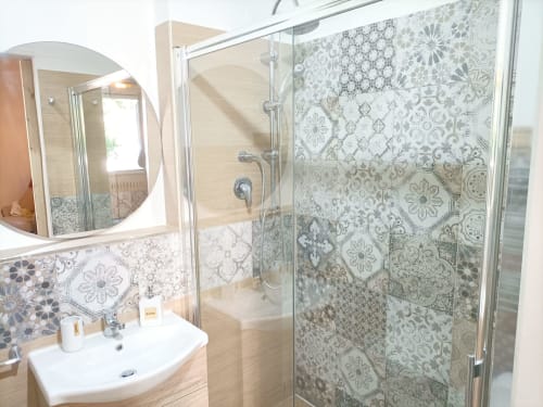 Moderno bagno della villa Newhouse a Bari con doccia in piastrelle decorate, specchio rotondo e lavabo