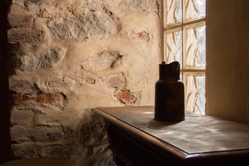 Rustic stone room at CasaRosada B&B in Vidracco with dark ceramic vessel on table by window