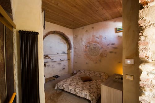 Rustic bedroom at CasaRosada B&B in Vidracco with arched doorway, patterned bedding, and exposed stone walls