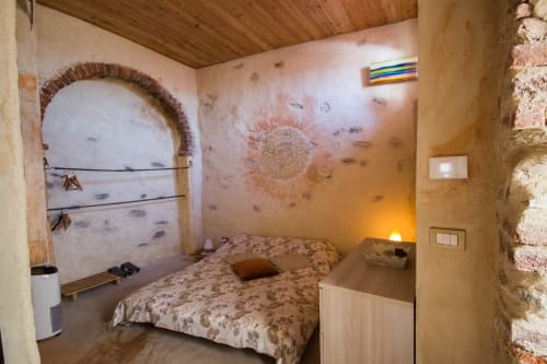 Rustic bedroom at CasaRosada B&B in Vidracco with arched doorway, patterned bedding, and warm terracotta walls
