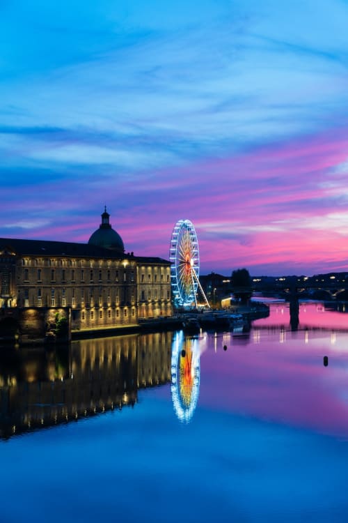Bord de Garonne à Toulouse au crépuscule avec la grande roue illuminée et bâtiment historique reflétés dans l'eau calme