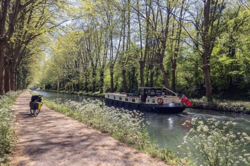 Chemin de halage du canal avec cycliste et péniche amarrée sur une voie navigable bordée d'arbres près de Toulouse