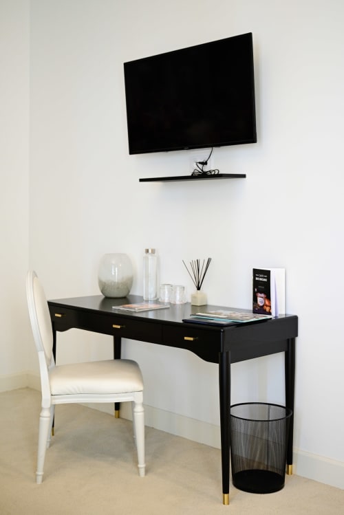 Modern black desk with white chair beneath wall-mounted TV at Pavillon Des Millesimes hotel in Lussac