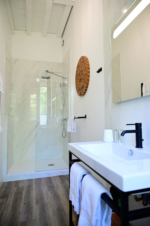 Modern bathroom at Pavillon Des Millesimes with marble shower, black faucet, and decorative wooden wall art in Lussac