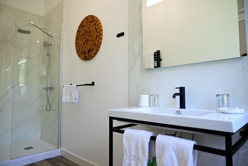 Modern bathroom in Lussac with marble walls, walk-in shower, white sink, black fixtures and wooden wall art