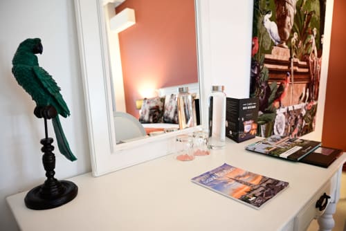Elegant vanity desk with green parrot statue, mirror, cosmetics, and travel guides at Pavillon Des Millesimes boutique hotel