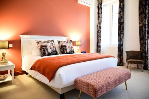 Chambre de luxe au Pavillon Des Millésimes avec mur d'accent orange, lit blanc, coussins décorés et banquette rembourrée