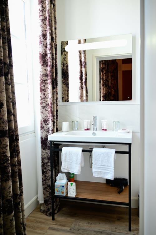 Modern hotel bathroom at Pavillon Des Millesimes with white sink, black vanity, illuminated mirror, and burgundy patterned