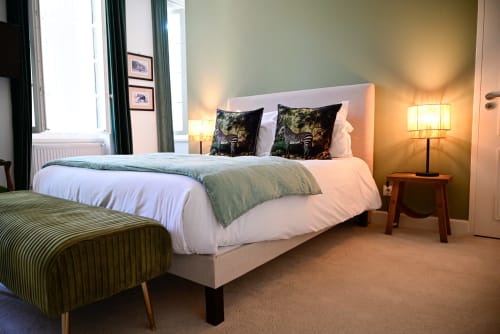 An elegant room at the Pavillon Des Millésimes featuring a wooden headboard, a palette of greens, a green armchair, and views of the pool and landscaped garden