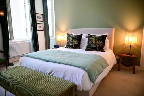 Chambre élégante au Pavillon Des Millésimes avec tête de lit en bois, camaïeu de verts, fauteuil vert et vue sur la piscine et le jardin paysagé