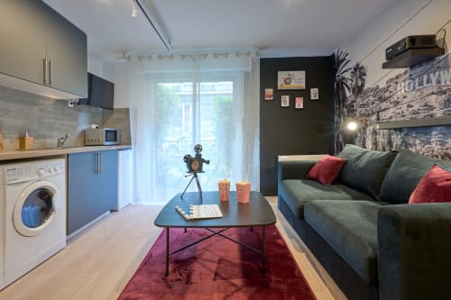 Cinema-themed studio apartment in Bordeaux with blue kitchen, gray sofa, and movie projector decor