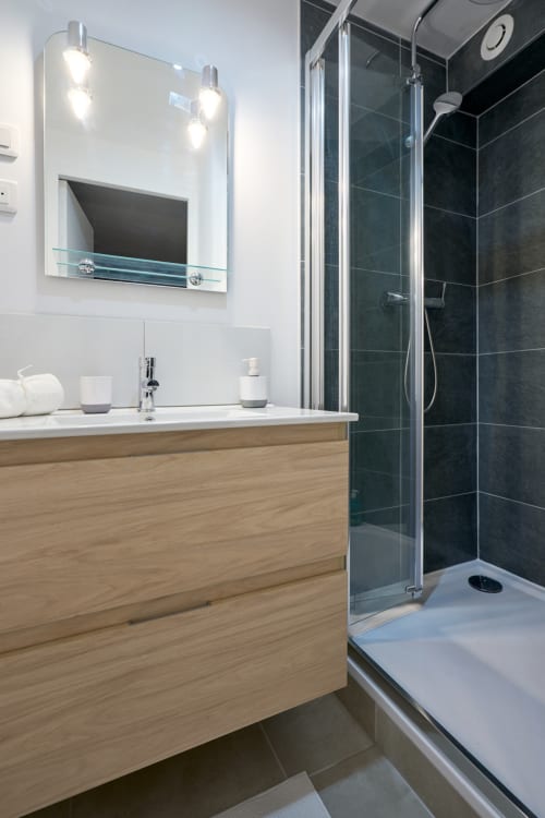 Modern bathroom in Bordeaux apartment with wooden vanity, illuminated mirror, and walk-in shower with dark tiles