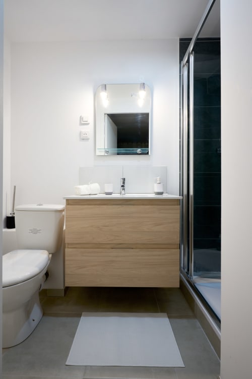 Modern bathroom with wooden vanity, white walls, mirror with lighting, toilet, and shower enclosure in Bordeaux apartment