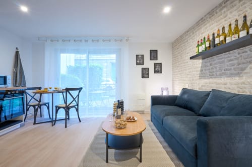 Modern studio apartment in Bordeaux with dark sofa, dining area, kitchenette, and wine bottles on shelf