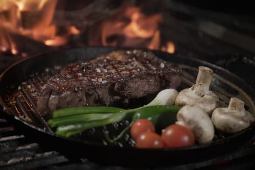 Bistecca alla griglia con funghi, scalogni verdi e pomodori in padella di ghisa sul fuoco da campeggio presso SleepWithMe luxury B&B a Pisa