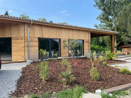 Extérieur de la salle d'événementiel en bois de l'hôtel des Chalets de Montréjeau avec sa verdure environnante.