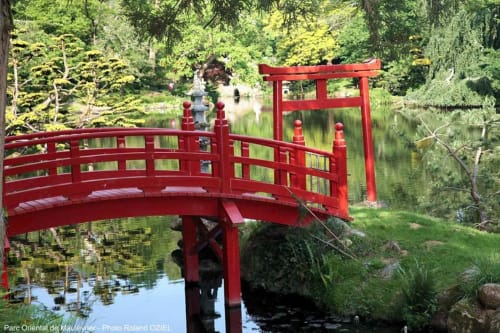 Pont rouge en arc au-dessus d'un bassin à La Maison D'olivier à Mesnard la Barotière, entouré de jardins luxuriants