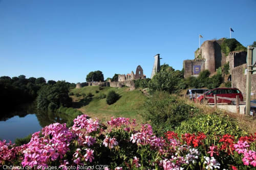 Château de Tiffauges avec des fleurs rose vif, pelouses verdoyantes, rivière et fourgonnette rouge garée à proximité