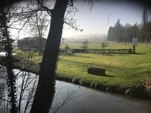 Peaceful riverside meadow at Les Gites De Flaubert with bare trees, green grass, and picnic area overlooking water