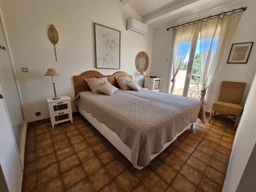 Helles Schlafzimmer in der Villa Sigahi mit Holzbett, weißen Nachttischen, Terrakottafliesen und Balkonblick in La Croix Valmer