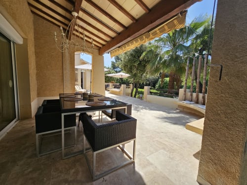 Überdachte Terrasse mit schwarzen Rattanmöbeln in der Villa Sigahi in La Croix Valmer, Palmen dahinter sichtbar