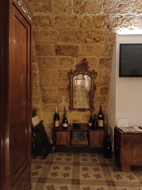Elegant hallway at CorteLirice Paradiso with stone walls, ornate mirror, wine bottles on dark wood console, and patterned