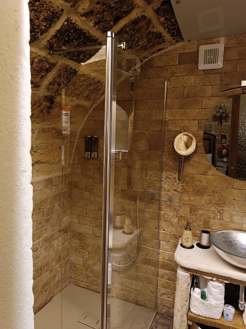 Modern bathroom shower with travertine tile walls at CorteLirice Paradiso apartment Sottano 2, featuring glass enclosure and