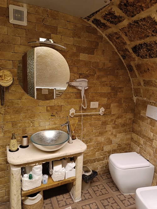 Modern bathroom in Sottano 2 apartment at CorteLirice Paradiso with brick walls, vessel sink, mirror, and toilet