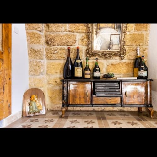 Wooden buffet with wine bottles and grapes against stone brick wall in CorteLirice Paradiso apartment