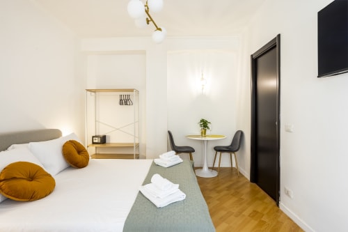 Camera moderna dell'Hotel Re di Roma a Roma con letto bianco, dettagli dorati, scrivania in legno e zona pranzo con vista sulla città