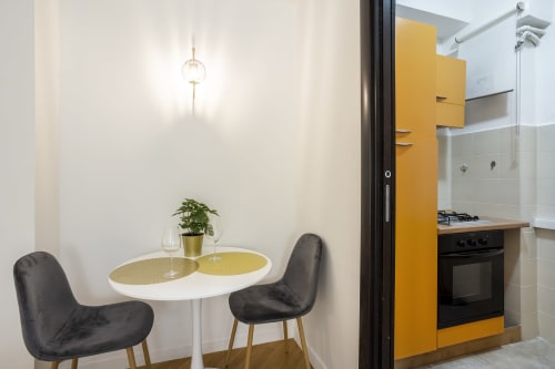 Zona pranzo moderna dell'hotel Re di Roma a Roma con accenti gialli, tavolo contemporaneo e vista sulla cucina aperta