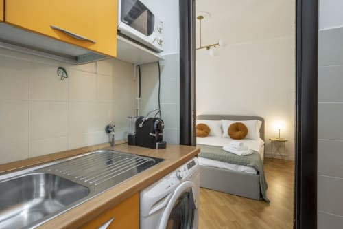 Moderno monolocale a Re di Roma con cucina gialla, lavatrice e camera da letto con cuscini dorati in vista