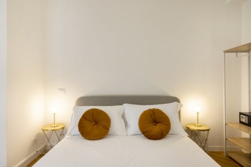 Camera da letto moderna dell'appartamento Re di Roma a Roma con testata grigia, biancheria bianca, cuscini rotondi dorati e comodini in ottone