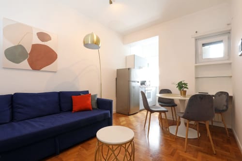 Moderno appartamento Re di Roma a Roma con divano blu navy, tavolo da pranzo e angolo cottura, arte contemporanea e dettagli in legno