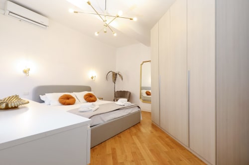 Camera da letto moderna dell'appartamento Re di Roma a Roma con letto grigio, dettagli oro e pavimenti in legno