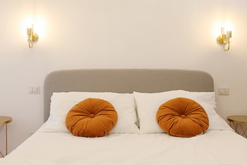 Camera da letto moderna dell'appartamento Re di Roma a Roma con cuscini arancioni rotondi, testata beige e applique dorate